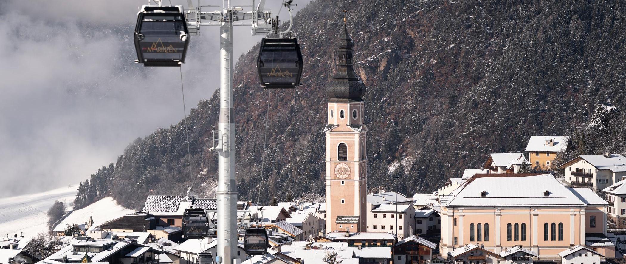 A view from the Marinzen gondola of snow-covered Kastelruth, with its church tower and the surrounding winter forests.