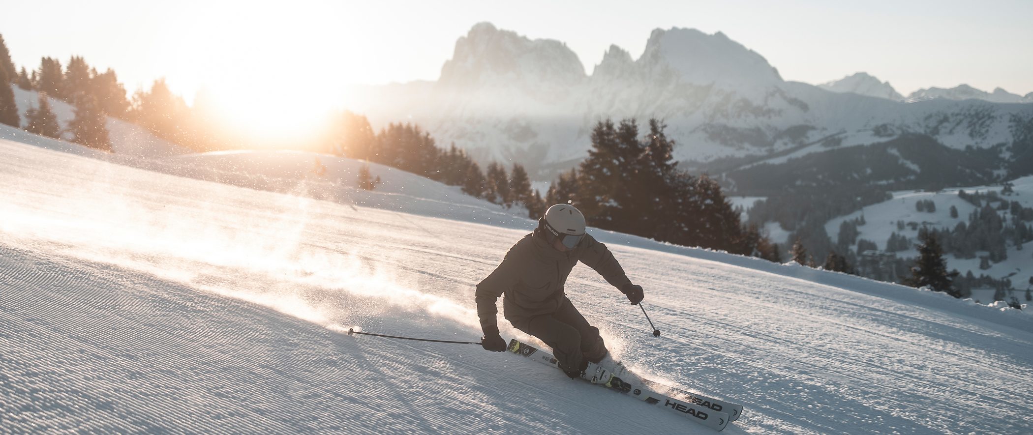 A skier carves turns on the slopes of the Seiser Alm in the morning, against the striking backdrop of the Langkofel and Plattkofel mountains in South Tyrol.