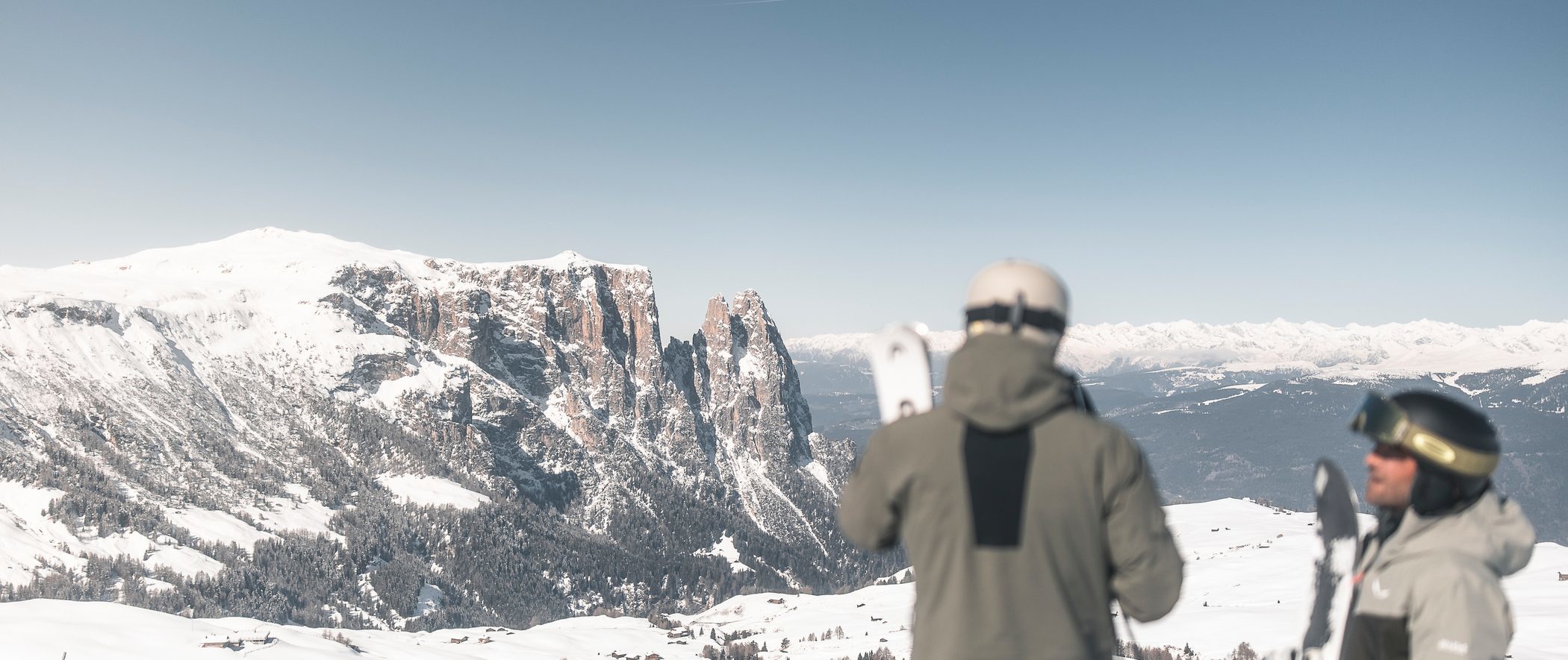 Skiers look out from the Seiser Alm toward the Schlern and the snow-covered mountain landscape.