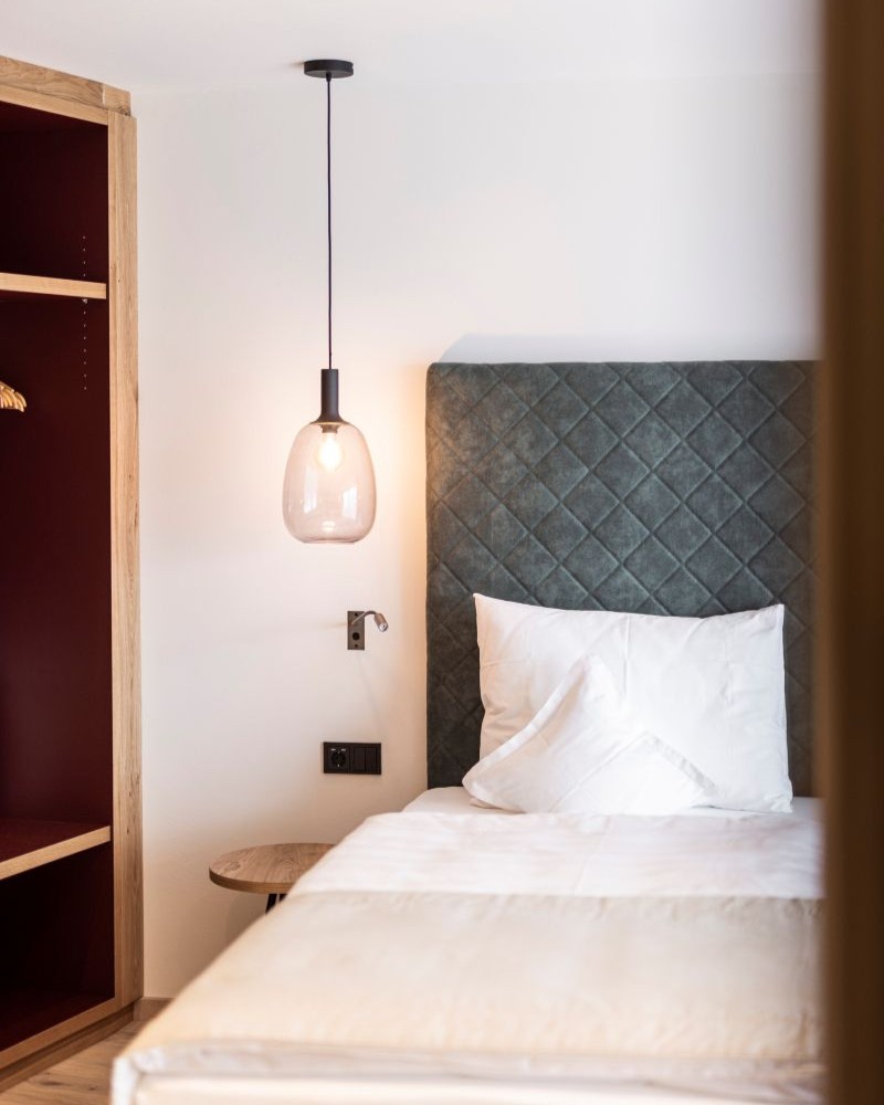 Accogliente camera dell'Hotel Baumwirt con letto imbottito moderno e arredamento in stile alpino.