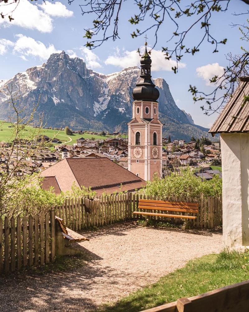 Vista su Castelrotto con il famoso campanile barocco e lo Sciliar sullo sfondo, incorniciati dal fresco verde primaverile.